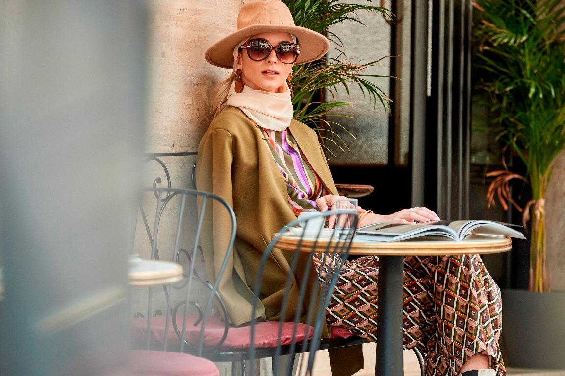 modella seduta indossa un elegante cappotto color cammello 